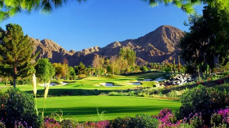 A scenic view of the golf course at Grand Hyatt Indian Wells, featuring well-manicured greens, sand bunkers, and a backdrop of lush trees and rolling hills.